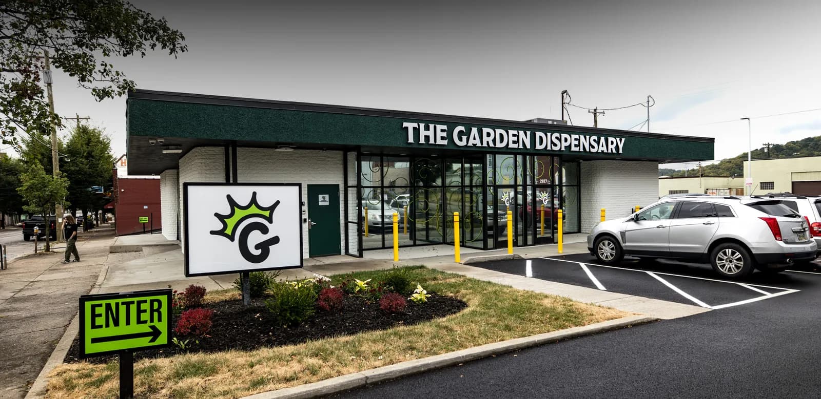 The Garden Dispensary in Camp Washington: the white storefront with its dark green band, the crowned G sign on the lawn and a lime ENTER arrow by the lot