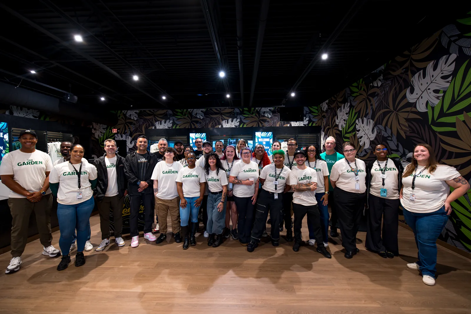 The Garden team in matching cream Garden tees on the sales floor, under the dark botanical mural