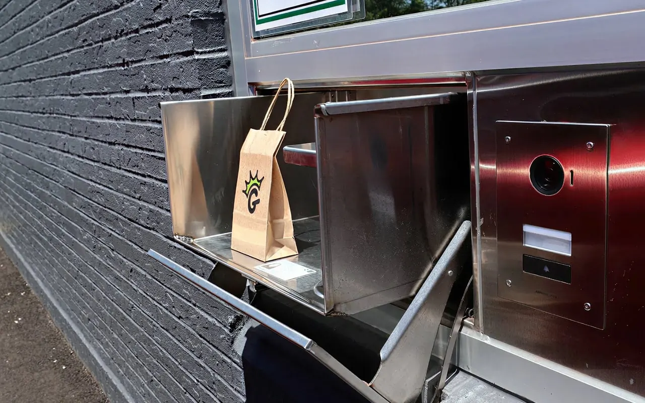 A crowned-G paper bag waiting in the stainless pickup drawer of The Garden drive-thru window