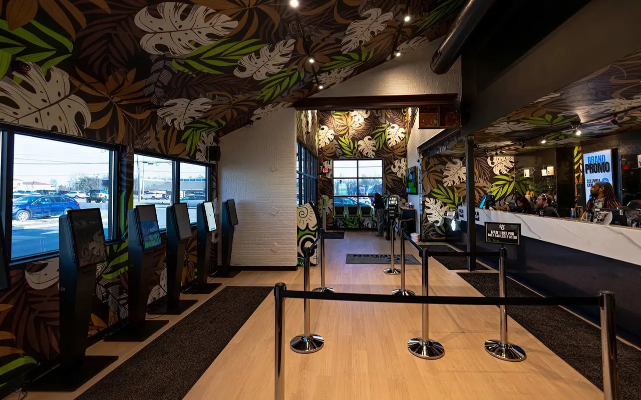 The Sycamore Township lobby: self-service kiosks under the Garden Jungle mural of monstera and palm leaves